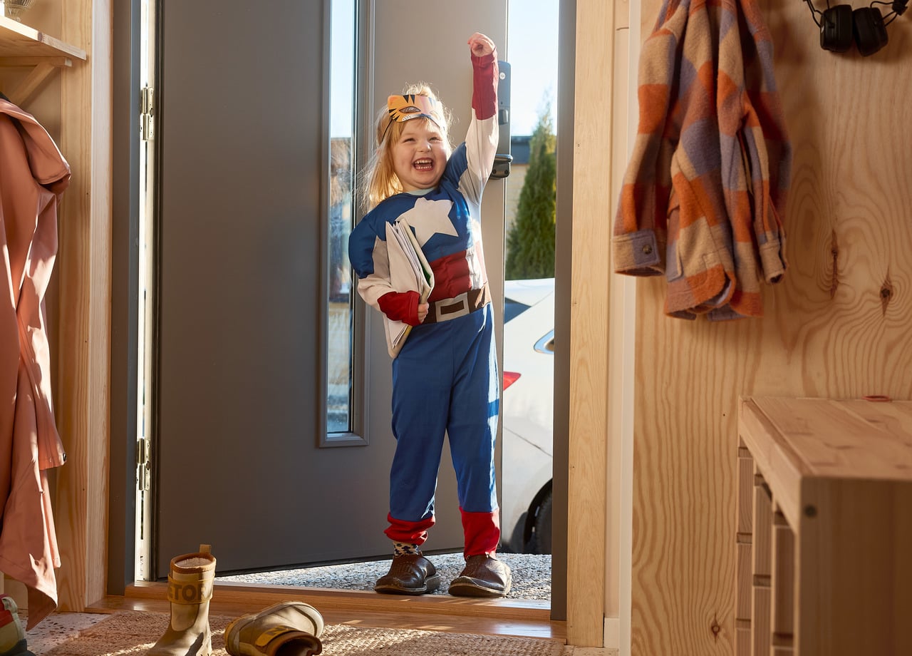 Flicka utklädd till superhjälte står i dörröppning.