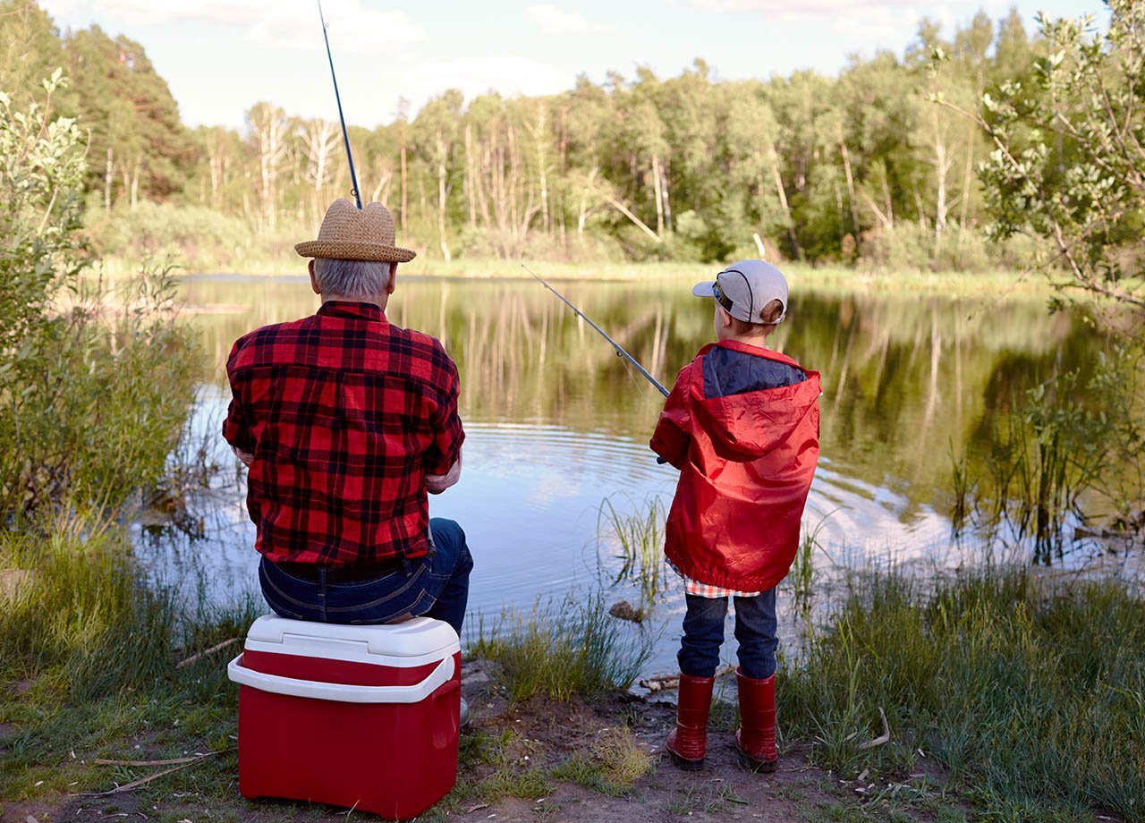 Man med hatt och pojke i keps fiskar i sjö.
