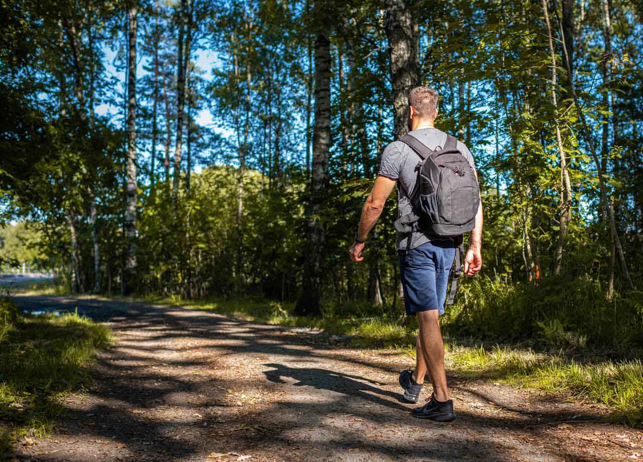 Man på promenad på väg i skog.
