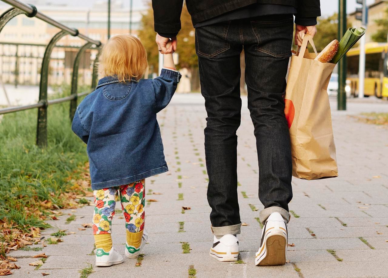 Pappa och dotter på promenad hållandes i handen med matkasse