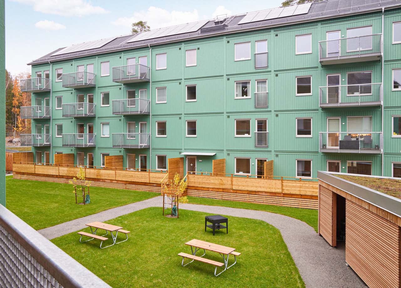 Foto på ett grönt fyravåningshus och en innergård med grön gräsmatta och sittbänkar