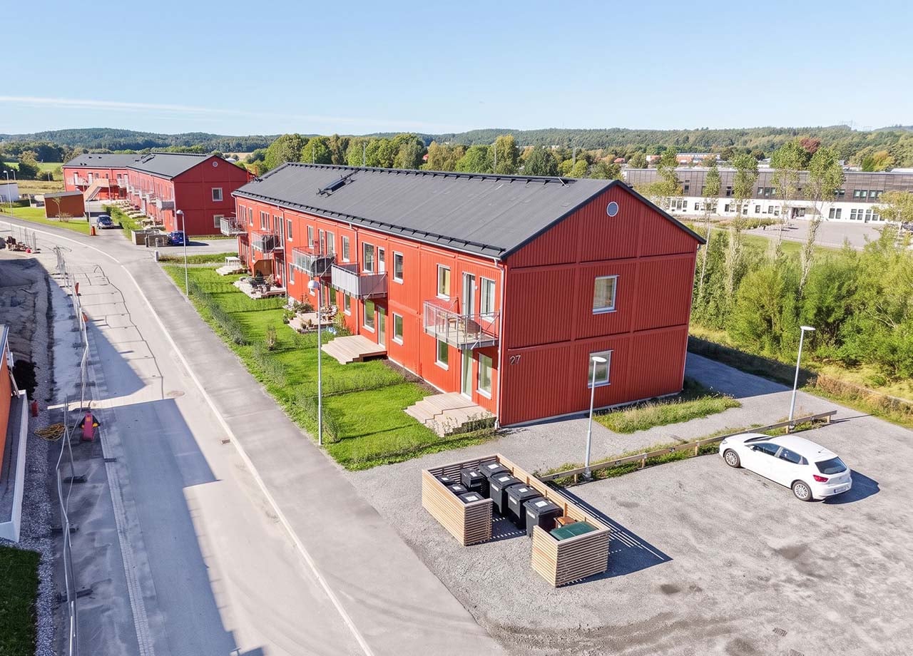 Flygfoto av altaner, balkonger och parkering till rött lägenhetshus i kvarteret BoKlok Klövern i Gråbo.