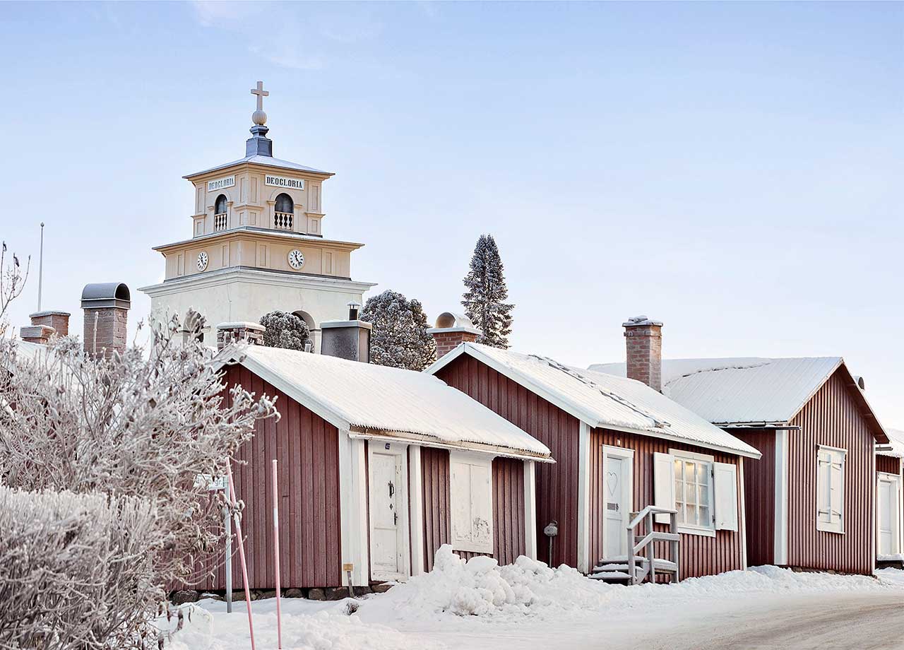 Foto på röda trähus och den gula kyrkan i Gammelstad, snötäckt.