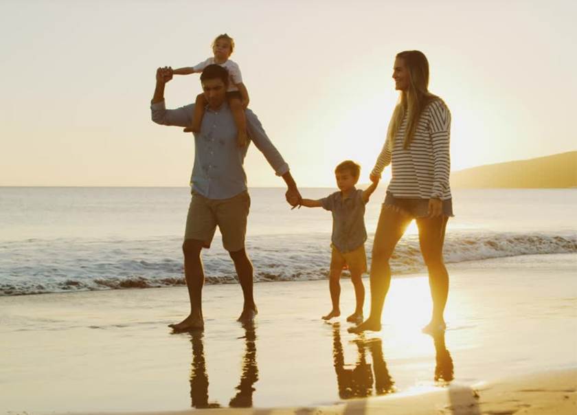 Familj om fyra på promenad på strand i solnedgång.